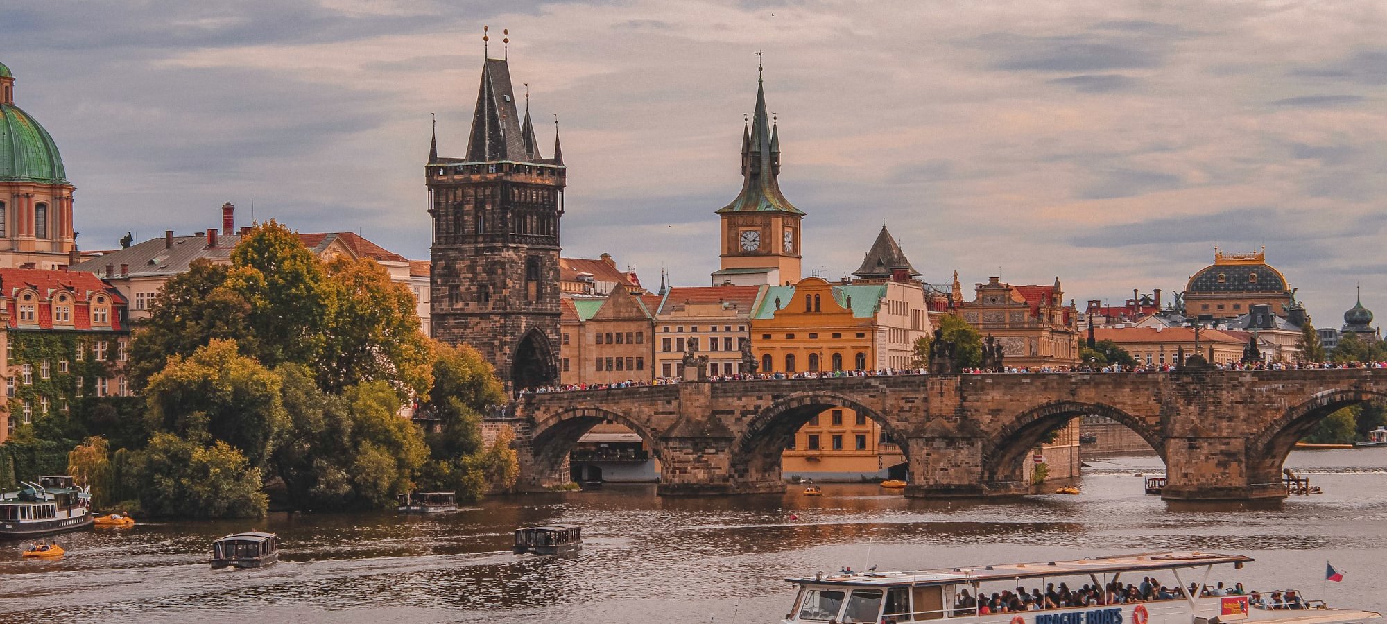 Charles Bridge over the Vltava with riverbank trees and moored boats
