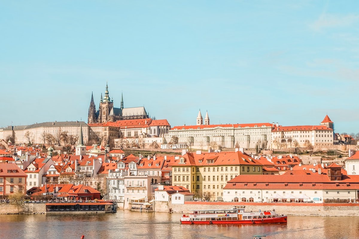 Prague Castle above a row of red-roofed riverside buildings